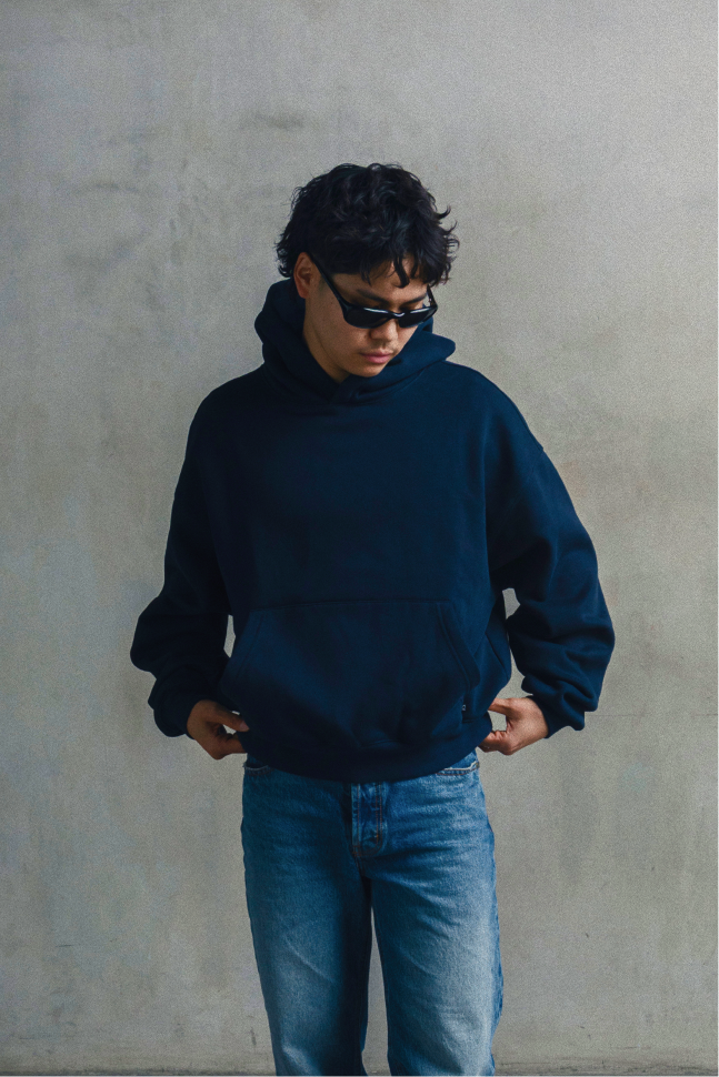 Model wearing a navy blue relaxed-fit hoodie with blue jeans, shown from the front.