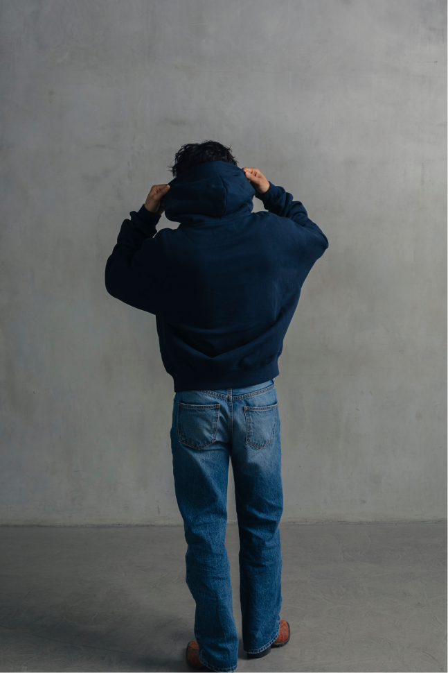 Back view of a model wearing a navy blue relaxed-fit hoodie with blue jeans while adjusting the hood.