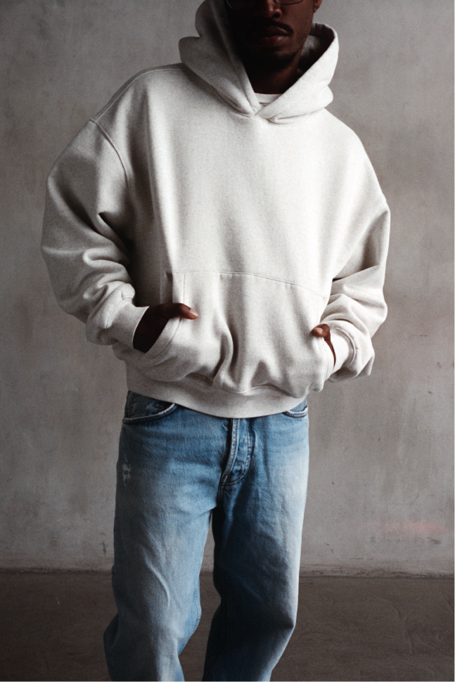 Close-up of a model wearing a light heather grey relaxed-fit hoodie with hands in the kangaroo pocket.