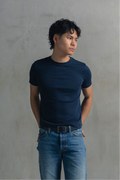 Model wearing a navy fitted crew neck T-shirt with blue jeans, looking to the side with hands behind the back.