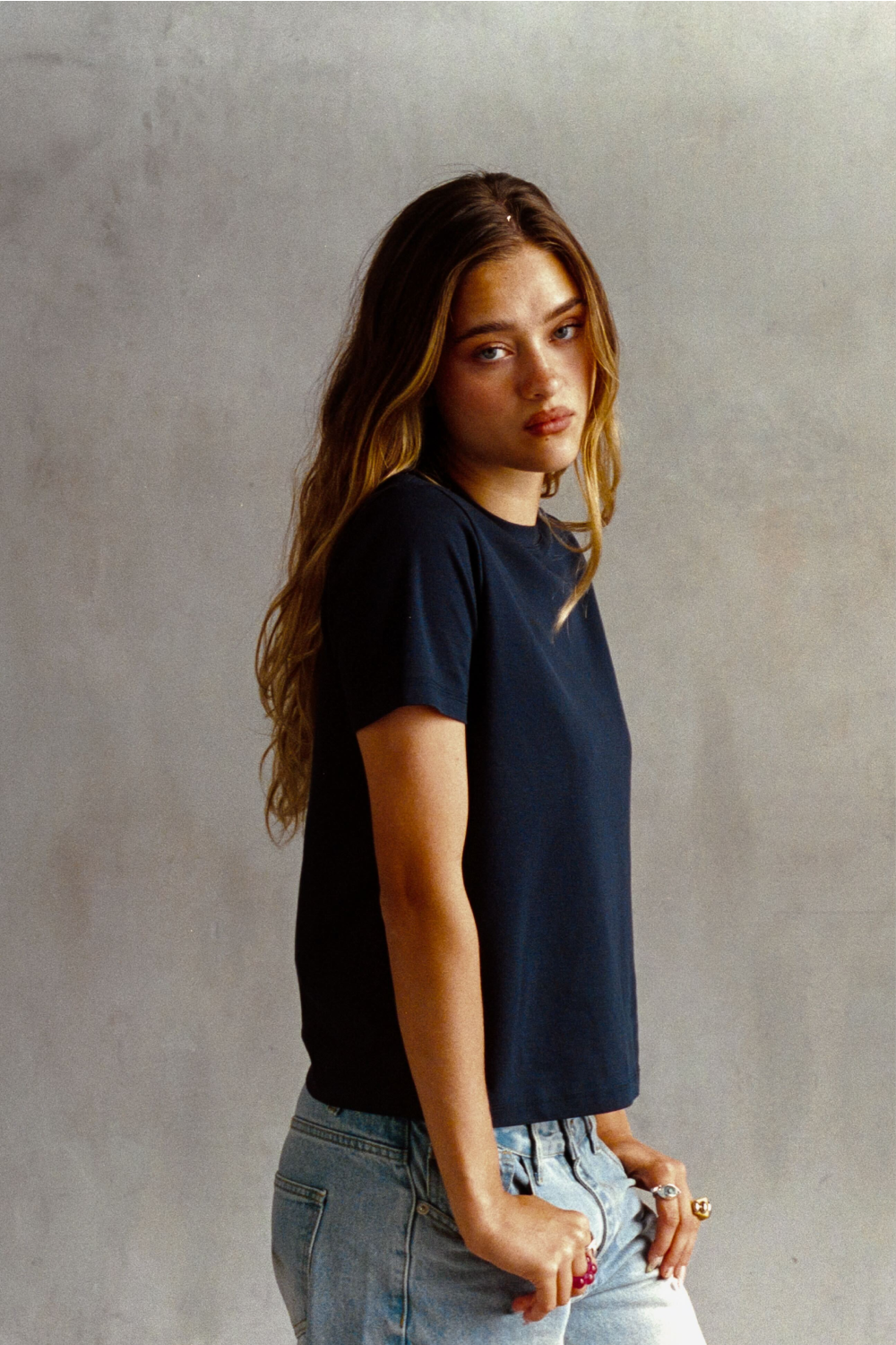 Model wearing a navy crew neck T-shirt with light blue jeans, shown from the side.
