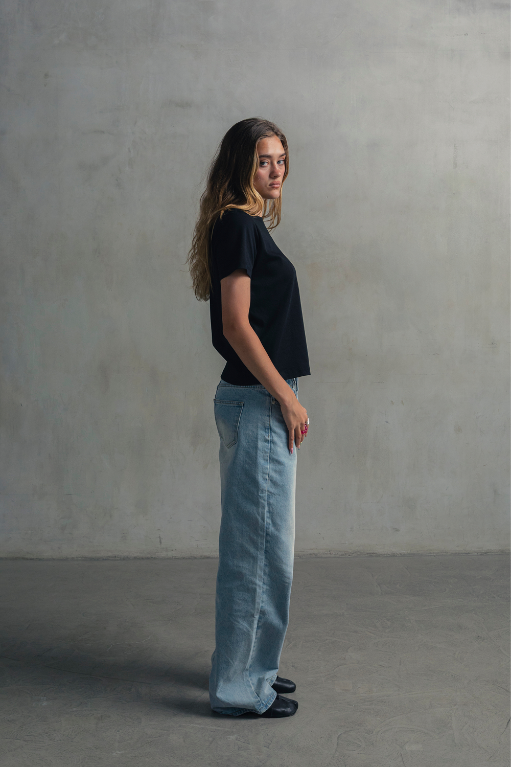 Model wearing a navy crew neck T-shirt with light blue jeans, shown from the side.